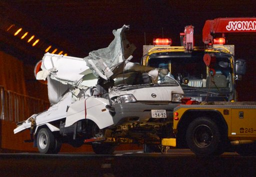 A tow truck hauls the wreckage of a truck, which was crushed in Sunday's accident, out of the Sasago Tunnel on the Chuo Expressway in Koshu, Yamanashi Prefecture, central Japan, early Monday, Dec. 3, 2012. Concrete ceiling panels fell onto moving vehicles deep inside the tunnel, and authorities confirmed nine deaths before suspending rescue work Monday while the roof was being reinforced to prevent more collapses. (AP Photo/Kyodo News)